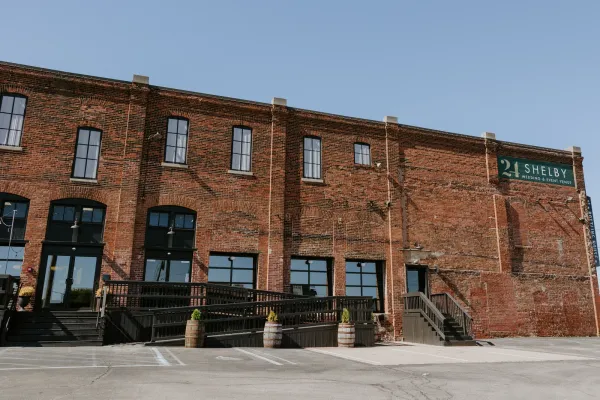 The 24 Shelby venue exterior on South Shelby Street in downtown Indianapolis, original 1898 bottling-house brick with modern garage doors lit warm at dusk.