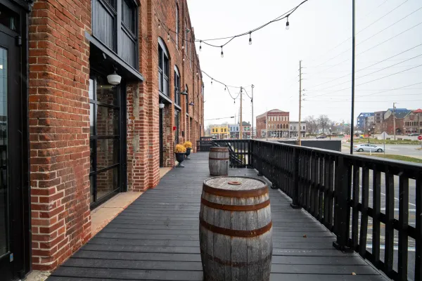 The Prohibition Patio at 24 Shelby, an outdoor wedding venue in Indianapolis, with string lights, wooden barrels, and the original 1898 brick facade of the historic downtown bottling house.