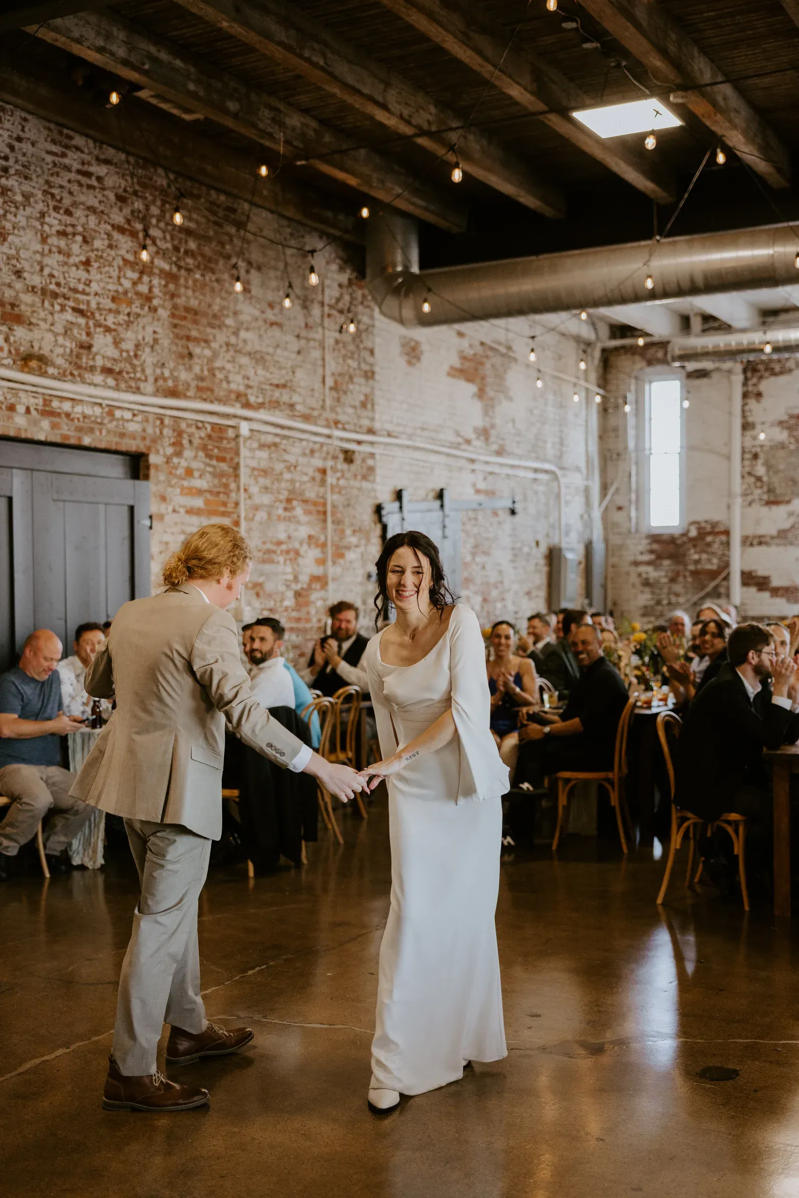 Wedding reception dance floor at 24 Shelby under Edison string lights and original wood-beam ceilings, with included lighting, sound, and stage that budget Indiana wedding venues almost never bundle into the rental.