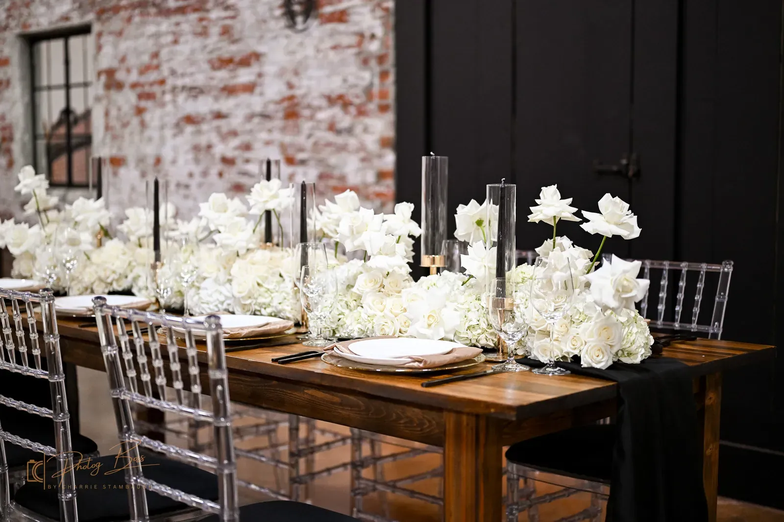 A black, gold, and ivory Art Deco tablescape at 24 Shelby with black taper candles, gold-rimmed chargers, white roses, and ghost chairs against the original 1898 brick, the Roaring Twenties wedding color palette in downtown Indianapolis